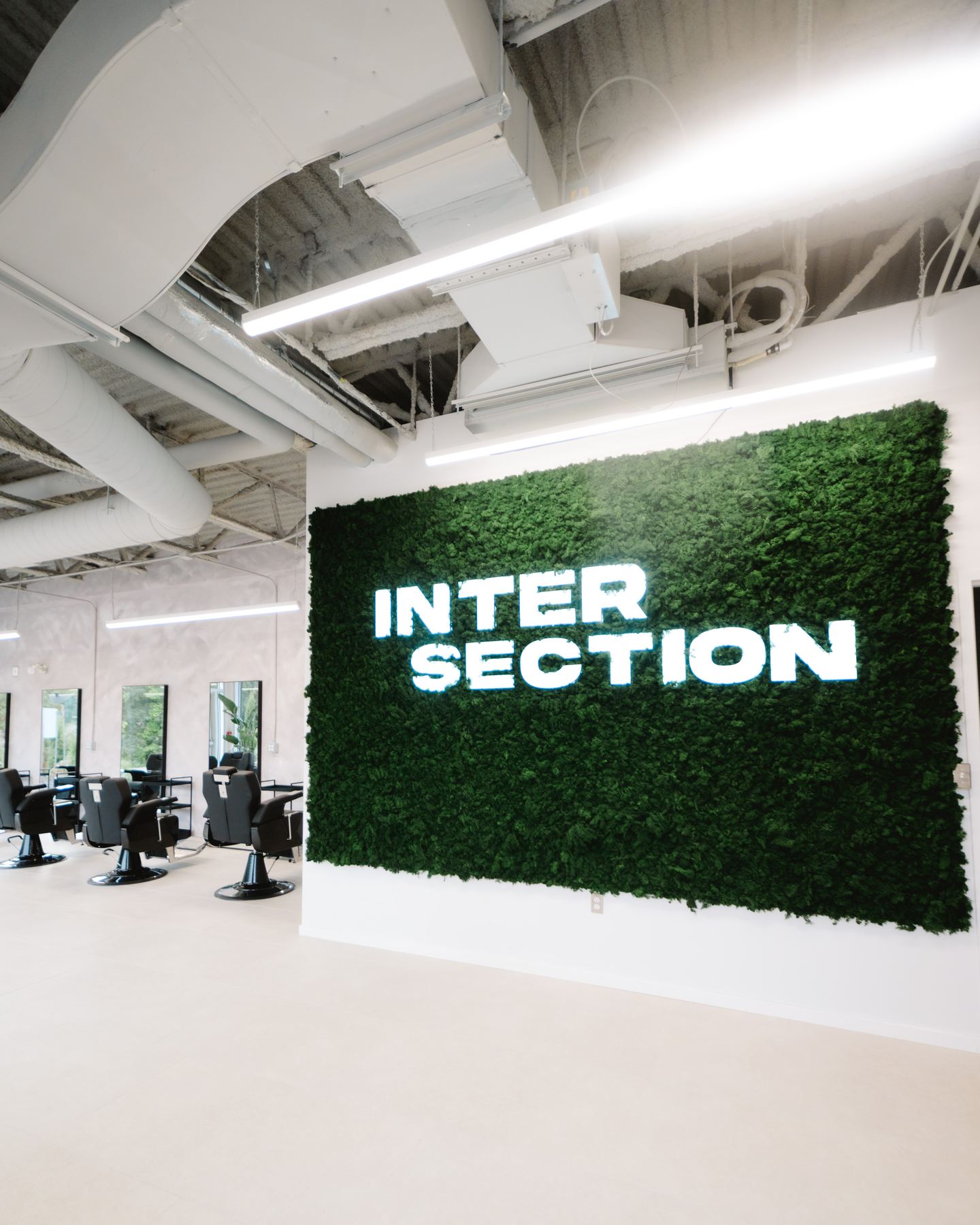 Intérieur d'Intersection Barbershop Chelsea — mur de mousse végétale avec l'enseigne lumineuse et les chaises de barbier